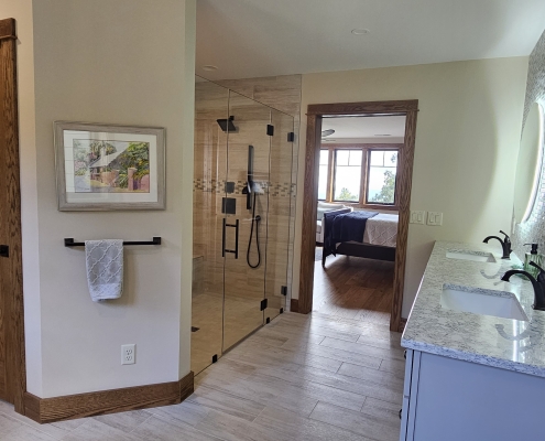 custom tile shower and vanity looking out of the bathroom door into the primary suite