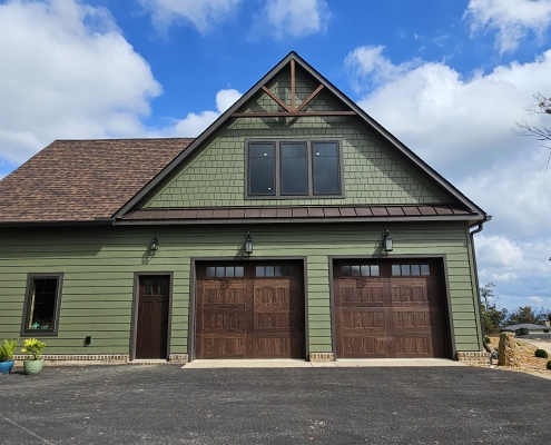 exterior garage wall showing green siding, wood garage doors and timber truss